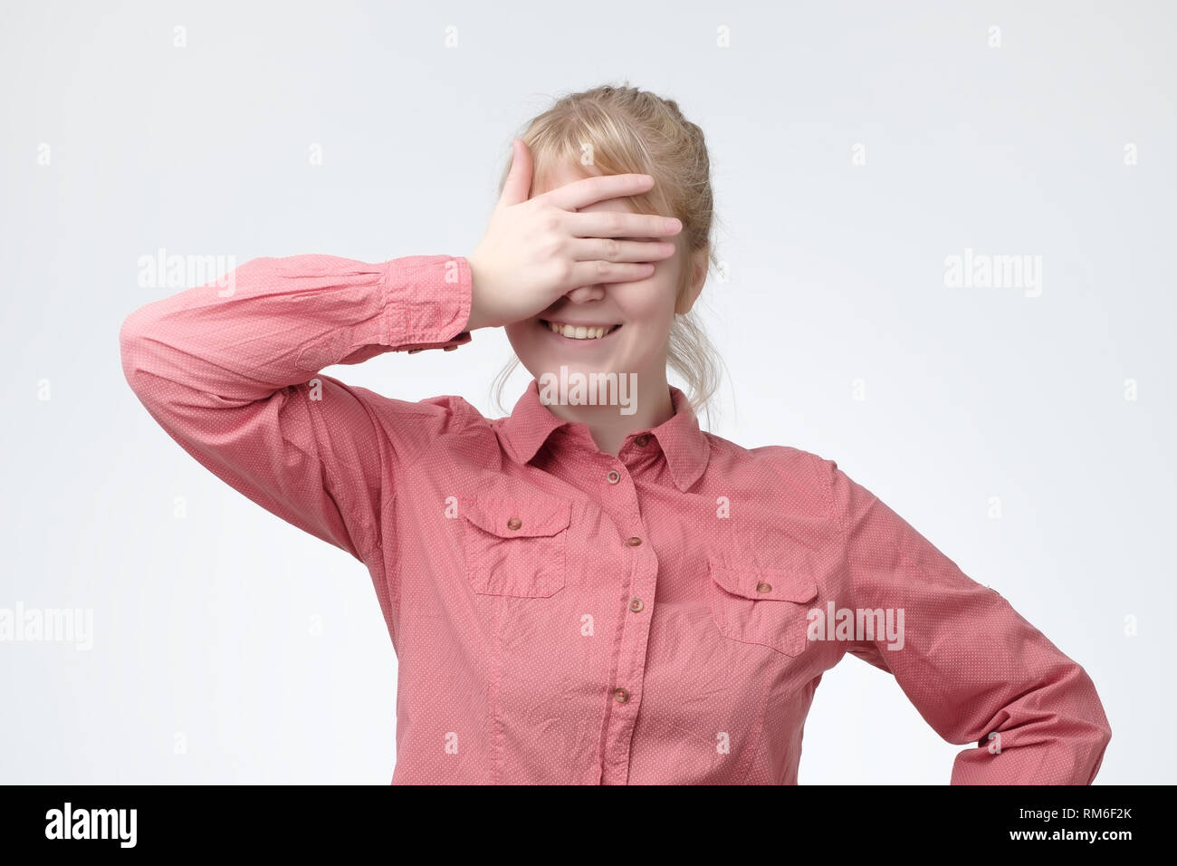Funny portrait of smiling blonde girl close her eyes with her hands, waiting for gift. Stock Photo