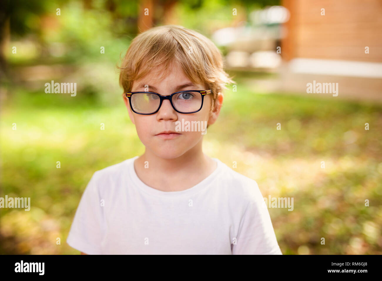 Blonde smiling boy with strabismus wearing glasses with special lens in  warm park Stock Photo - Alamy