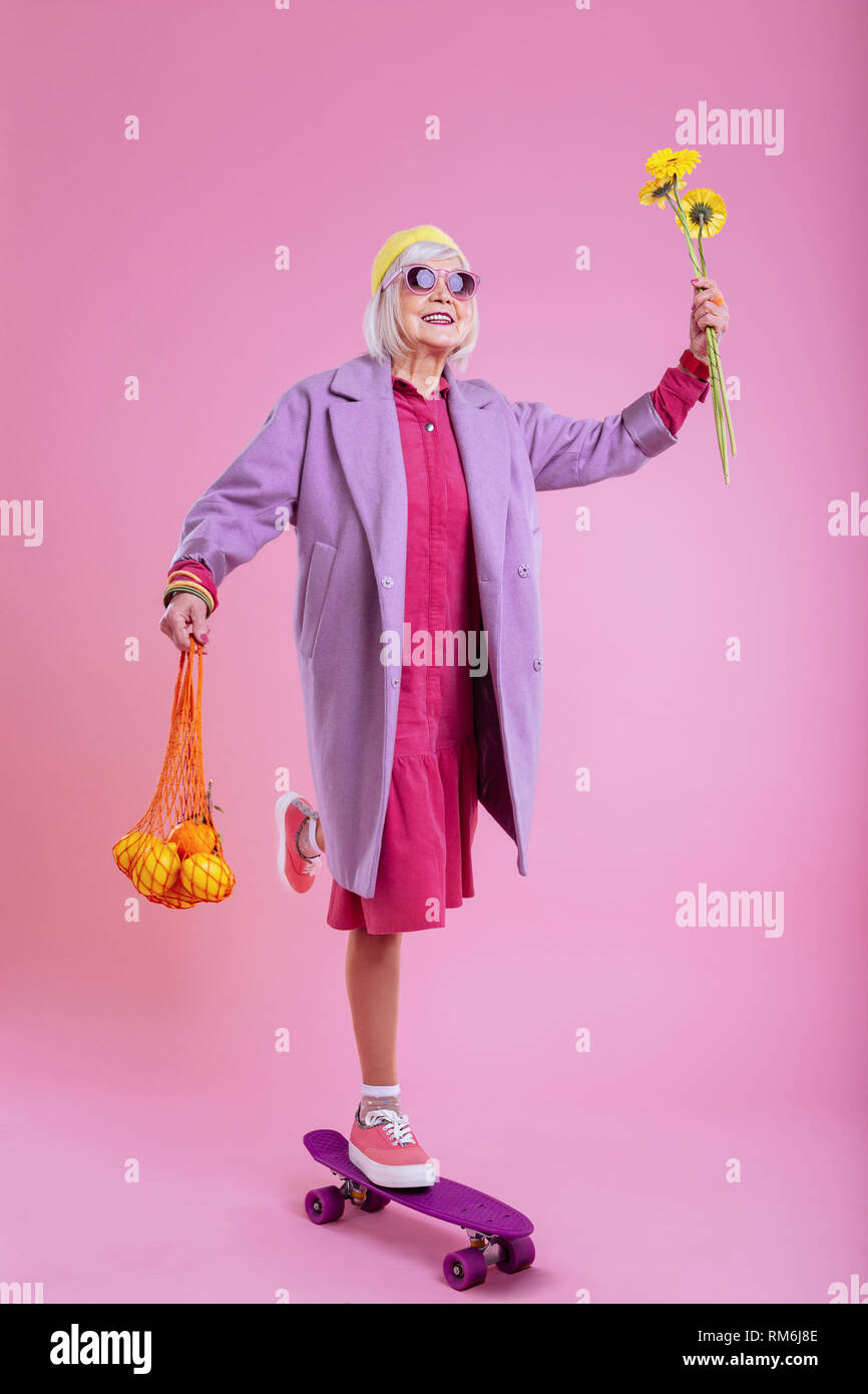 Elderly lady standing on skate holding sunflowers and fruits Stock Photo