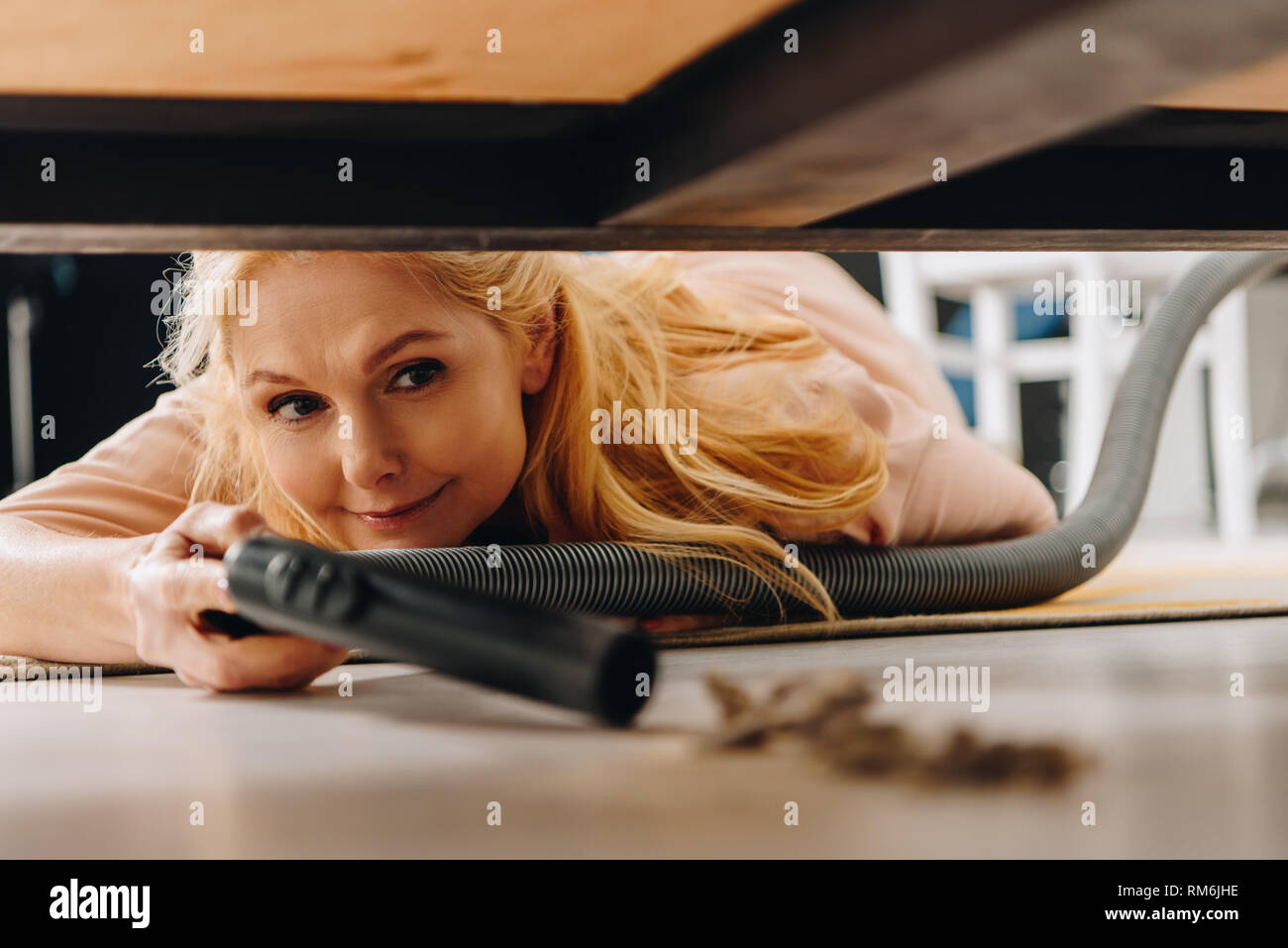 Smiling senior woman using vacuum cleaner under furniture Stock Photo