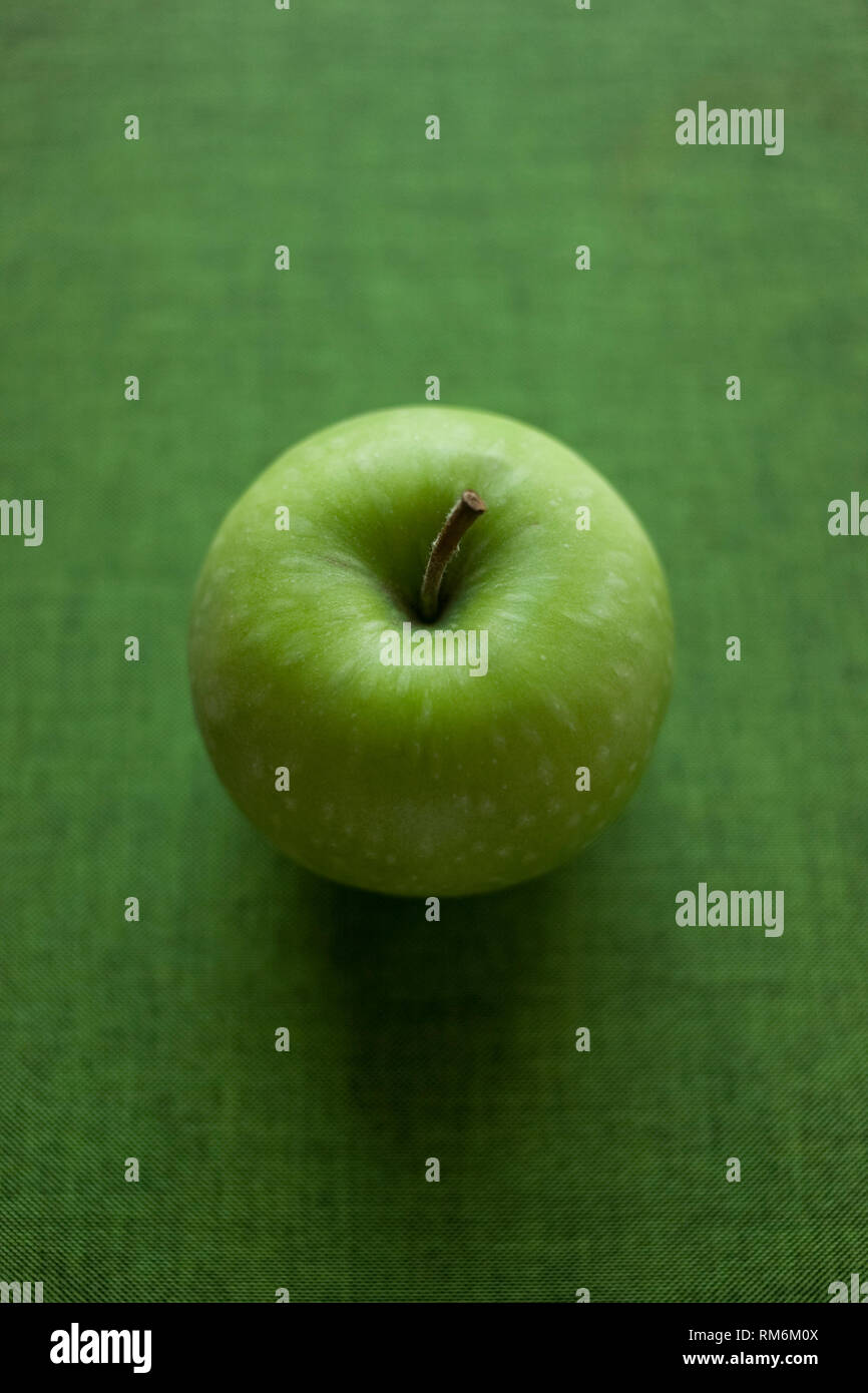 A Single Green Apple On A Green Textured Background Stock Photo