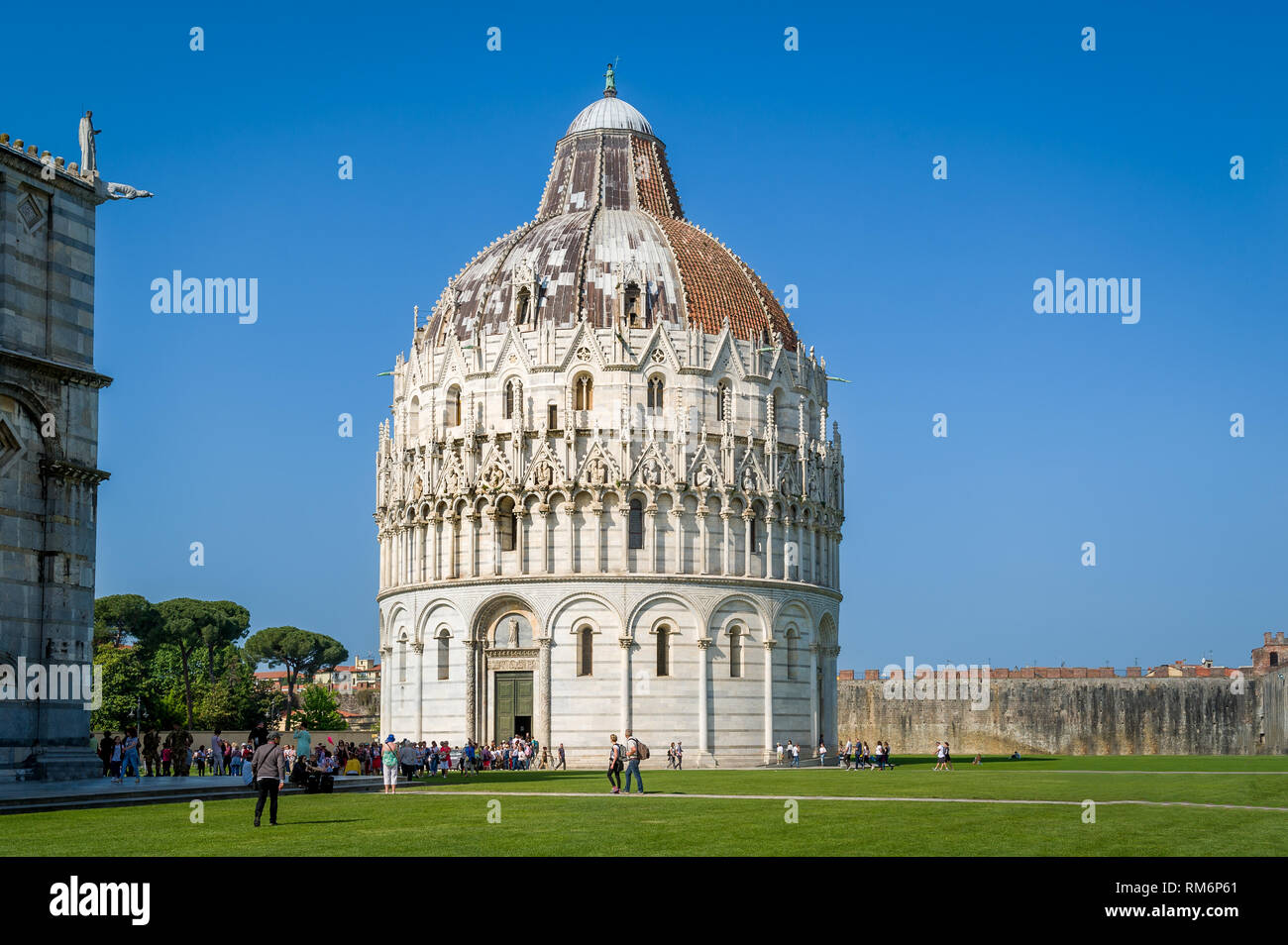 Pisa Baptistery beautiful decorated historic tower and tourists walking at the central square of Pisa. Tuscany, Italy. Stock Photo