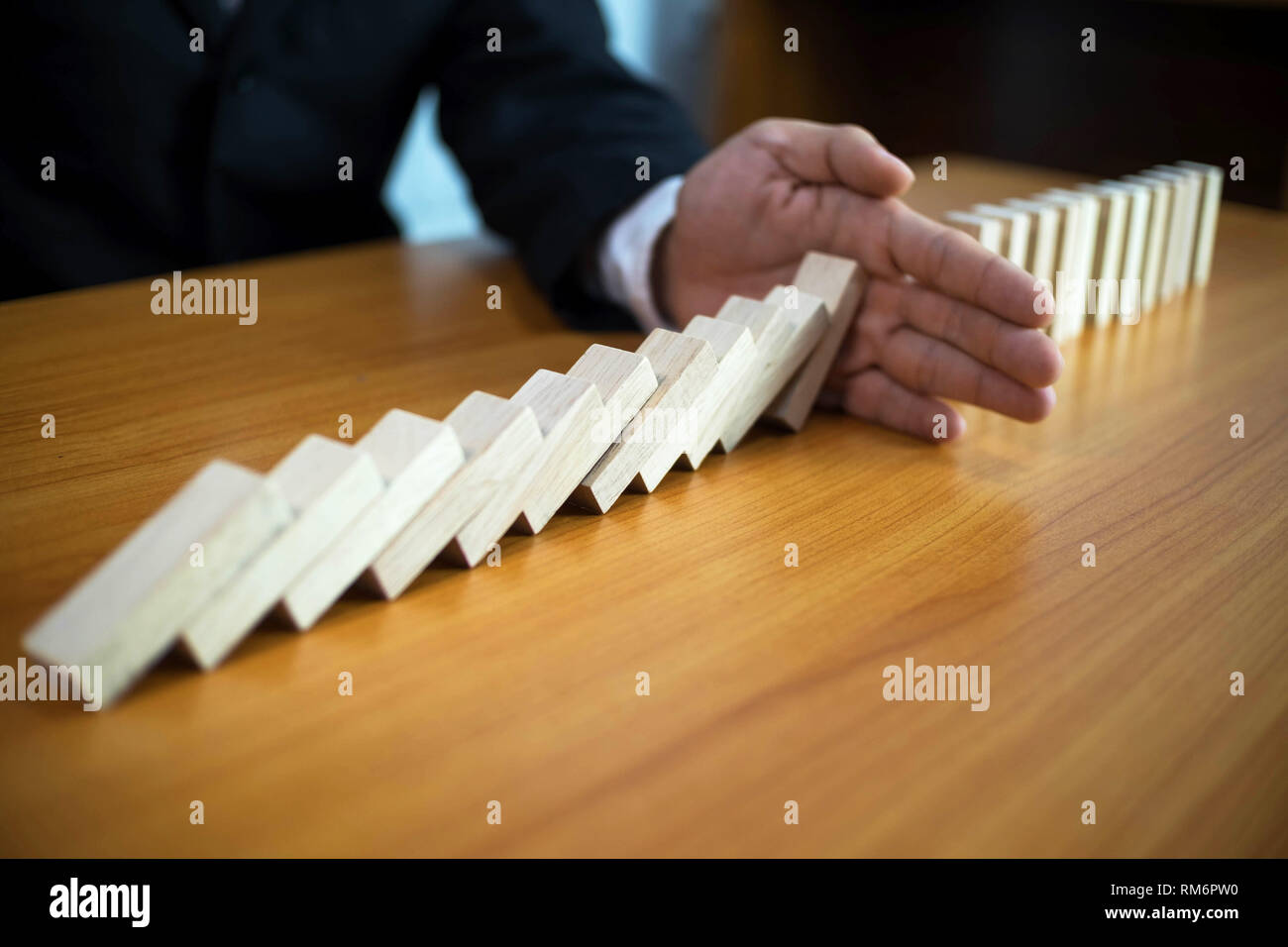 Businessman hand stops domino continuous overturned meaning that hindered business failure. Stop over this business failure concept. Stock Photo
