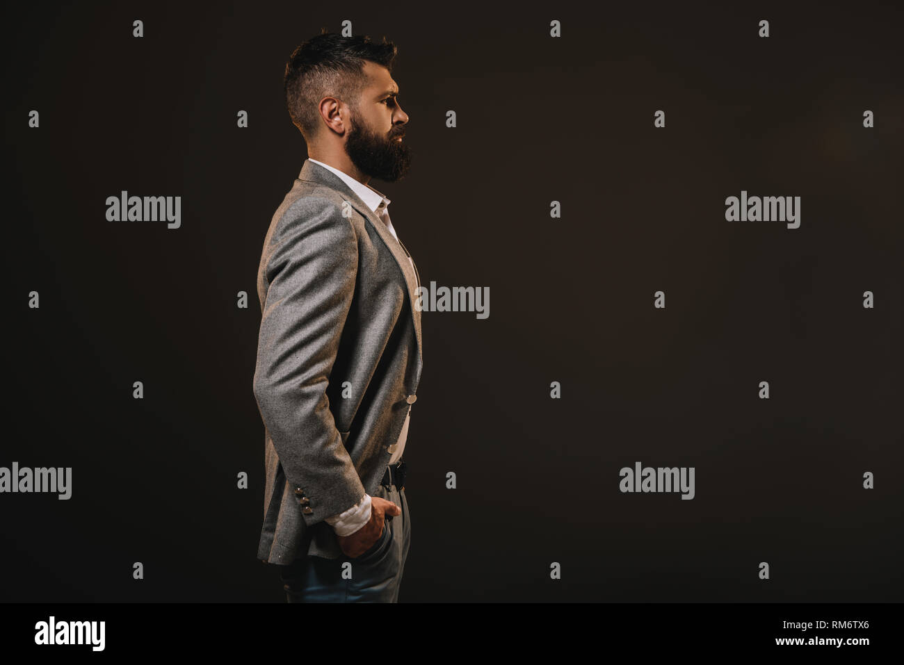 side view of beard businessman posing in gray jacket isolated on brown Stock Photo