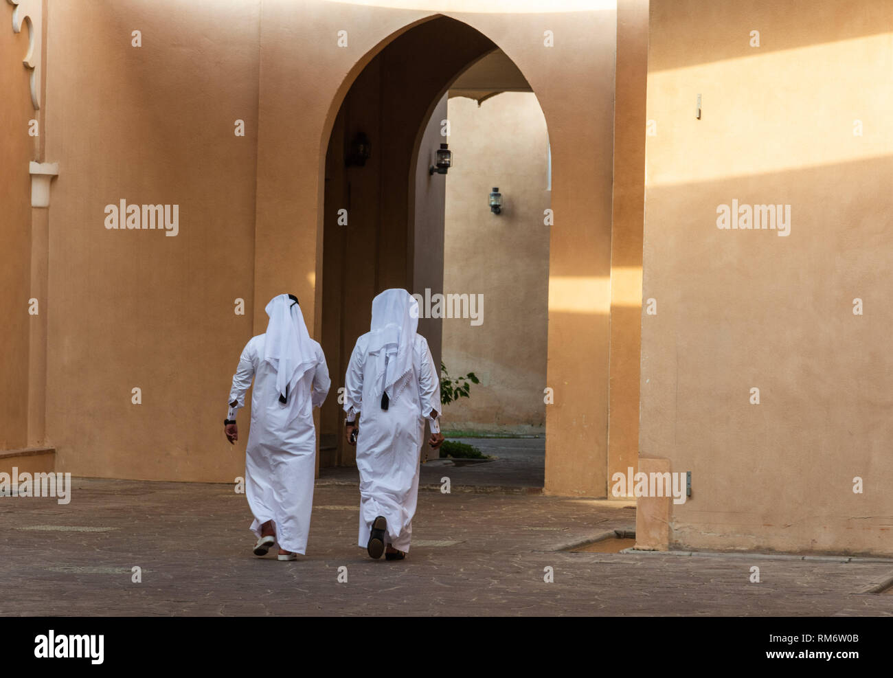 Two unidentifiable Arabic men in white thobe clothing walking away in Doha, Qatar. Stock Photo