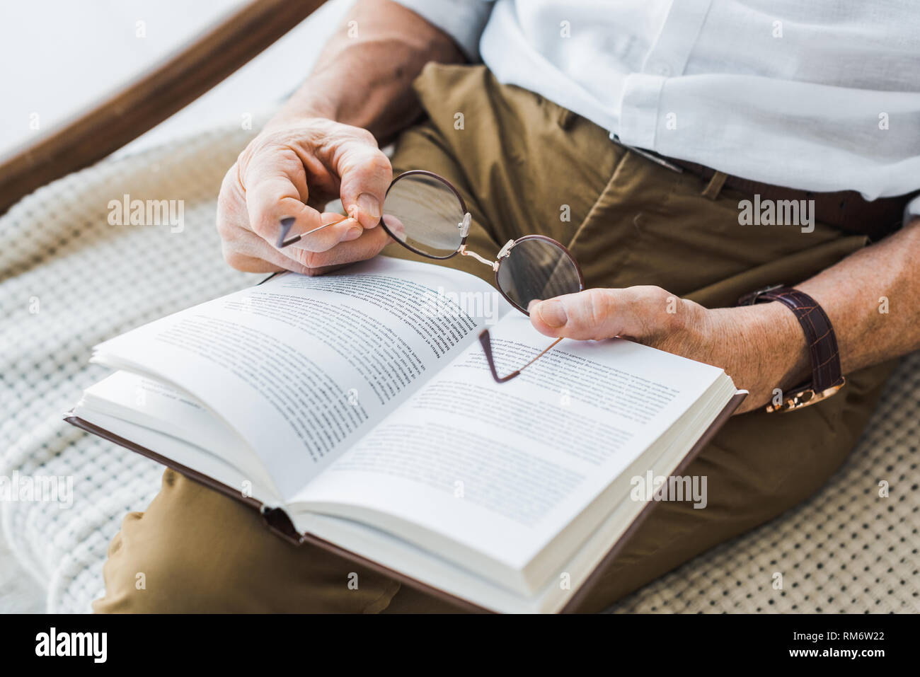 cropped view of senior man reading book and holding glasses at home Stock Photo