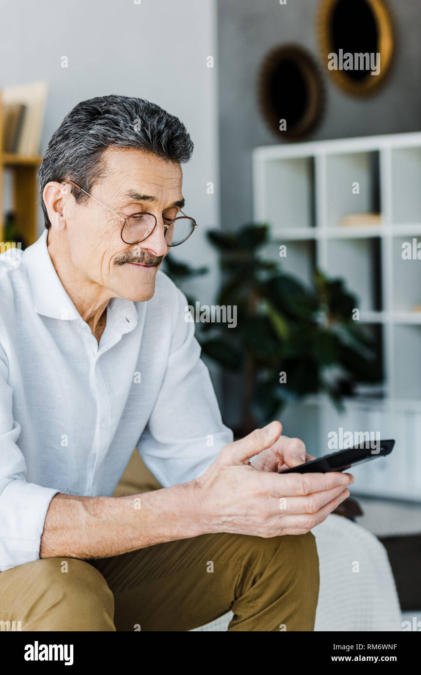 senior man with mustache looking at remote control in hands Stock Photo