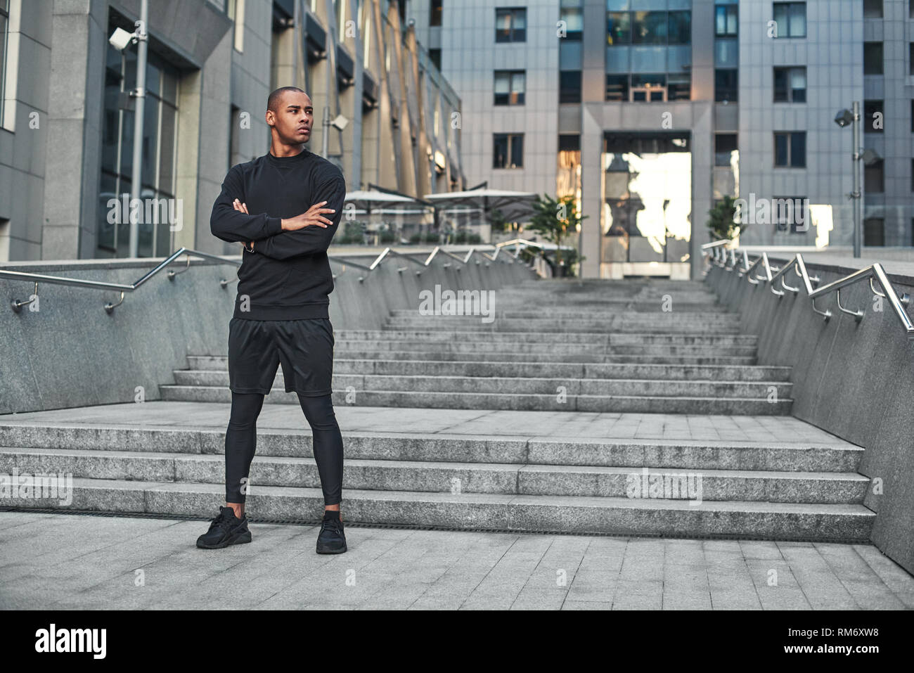 Confident in his body. Full length portrait of athletic african man with a muscular body standing on stairs with crossed arms and ready to start his morning workout. Healthy lifestyle. Sport motivation concept. Fitness concept. Stock Photo