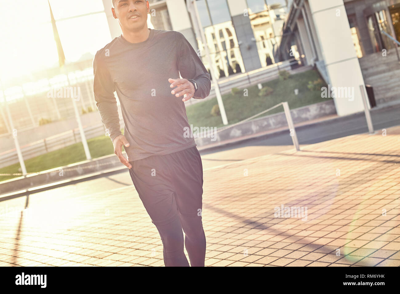 Perfect sunny morning. Young smiling african man in sportswear enjoying sunny morning while doing cardio training outside. Healthy lifestyle. Sport motivation concept. Fitness concept. Stock Photo