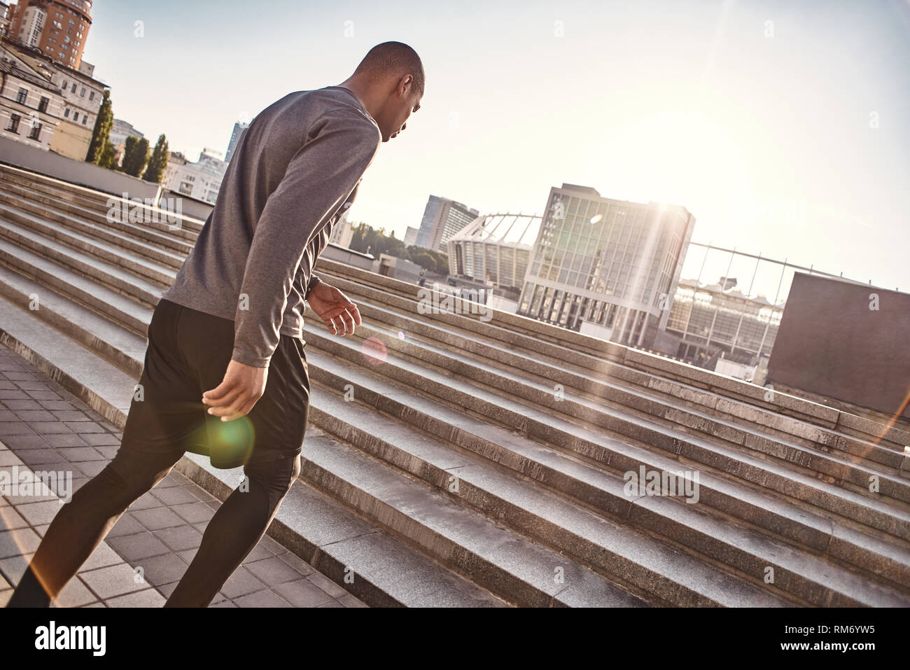 Urban workout. Back side photo of athletic african man in sportswear going upstairs while his morning training. Healthy lifestyle. Cardio training. Urban workout. Sport motivation concept. Stock Photo