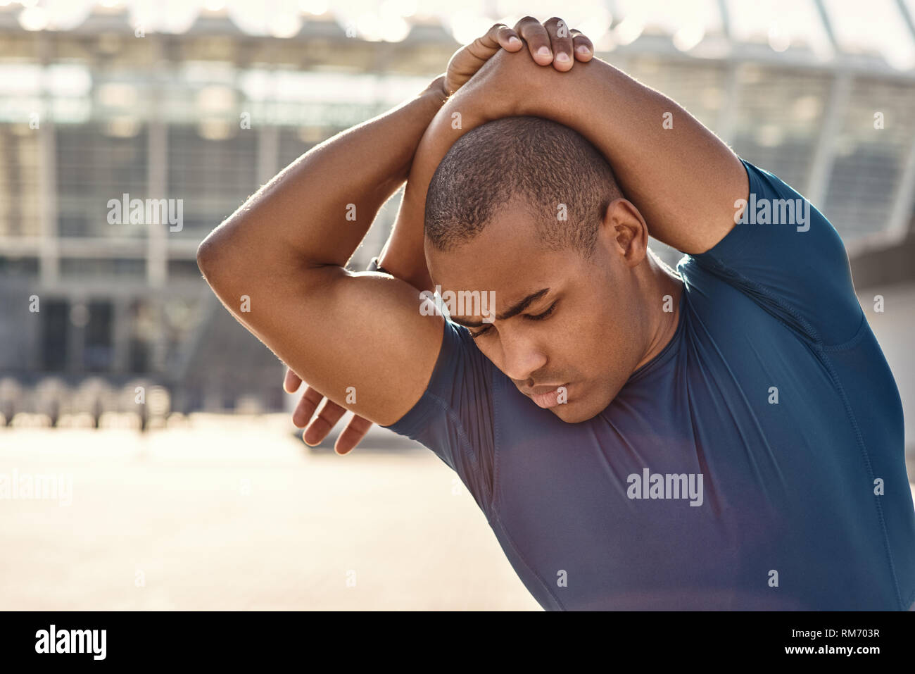 Feel your muscles. Close up portrait of athletic african man standing outside and stretching his arms before training. Cardio training. Healthy habits. Sport motivation concept. Fitness concept. Stock Photo