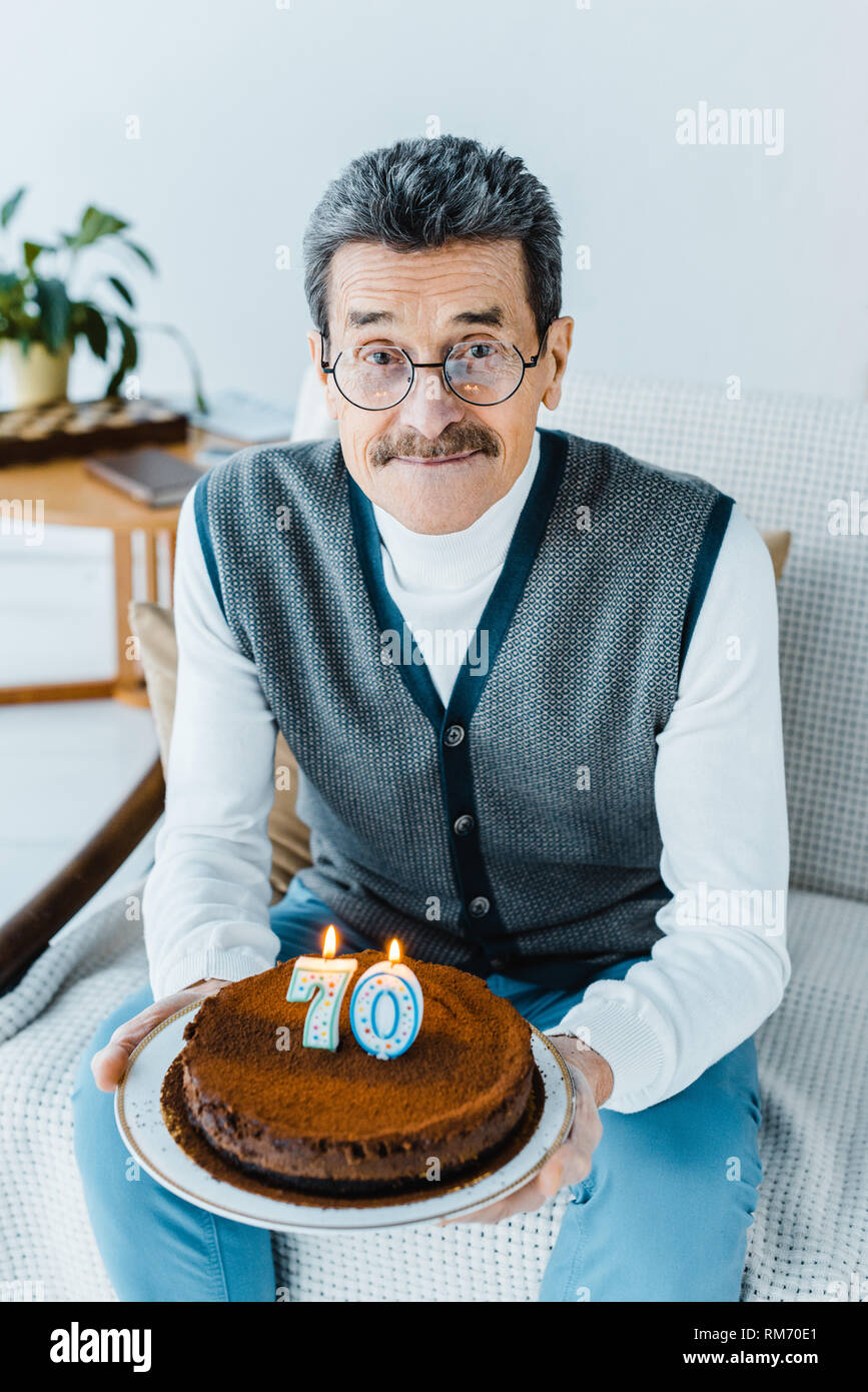 happy senior man holding birthday cake while sitting on sofa a in living  room Stock Photo - Alamy