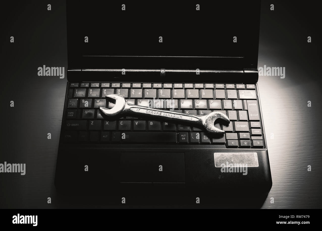 Opened old laptop on white table and metal wrench as concept of servicing. Stock Photo