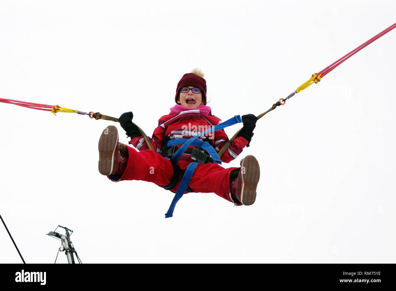 Little girl bungee jumping on trampoline during winter festival Stock Photo