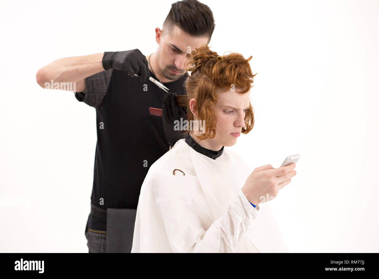 Young man browsing at his phone, while getting a haircut Stock Photo
