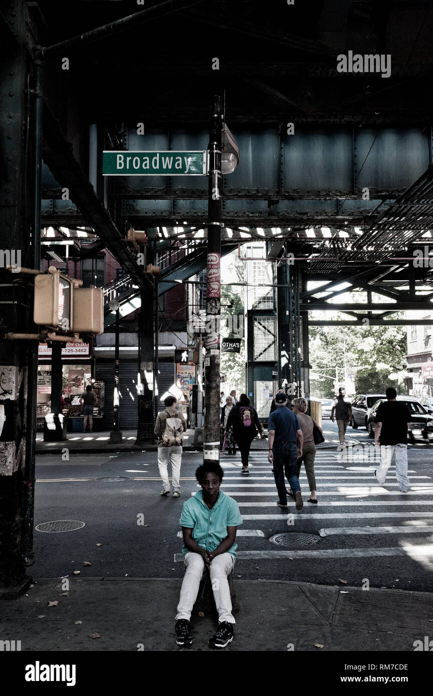 A black woman sitting at busy crossing under overhead subway line the bronx with broadway sign above New York city USA Stock Photo