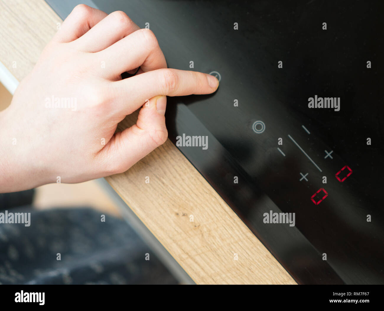 Dangerous situation in the kitchen. Child playing with electric glass-ceramic cooktop stove. Stock Photo