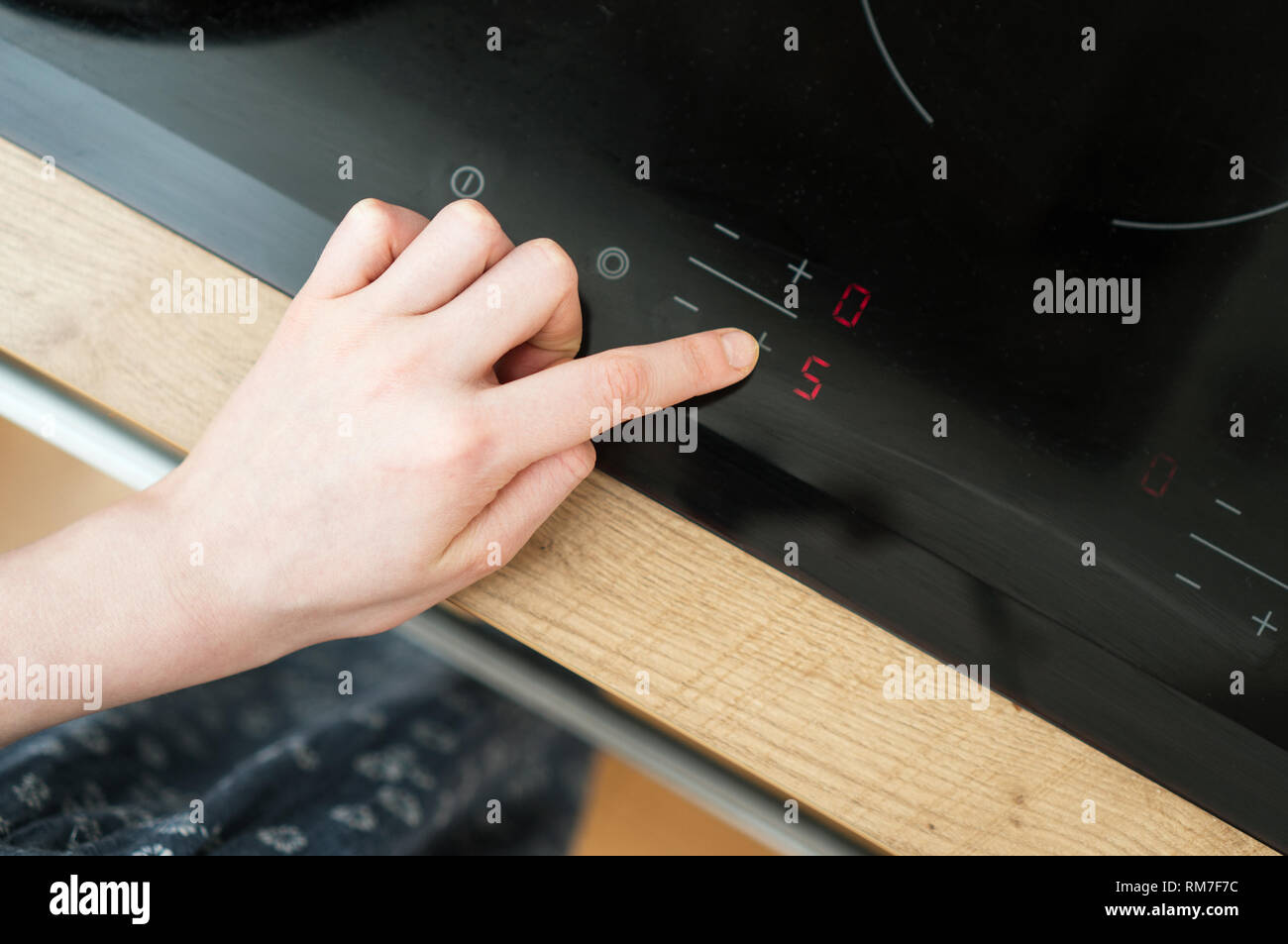 Dangerous situation in the kitchen. Child playing with electric glass-ceramic cooktop stove. Stock Photo