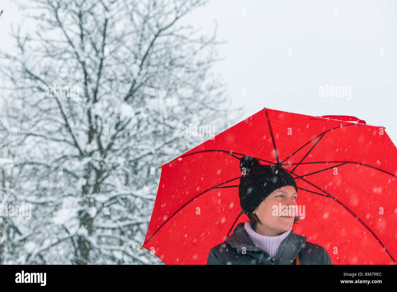 Sad disappointed woman in standing in winter snow under big red umbrella Stock Photo