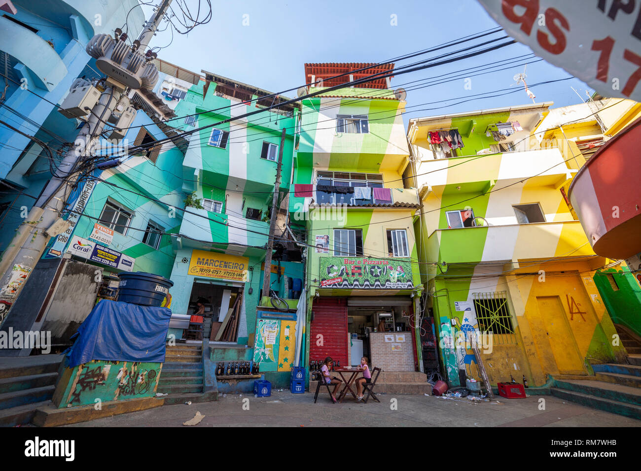 Colourful main square of the favela Santa Marta (Dona Marta) in Rio de Janeiro with two girls sitting at a table in front of a bar Stock Photo