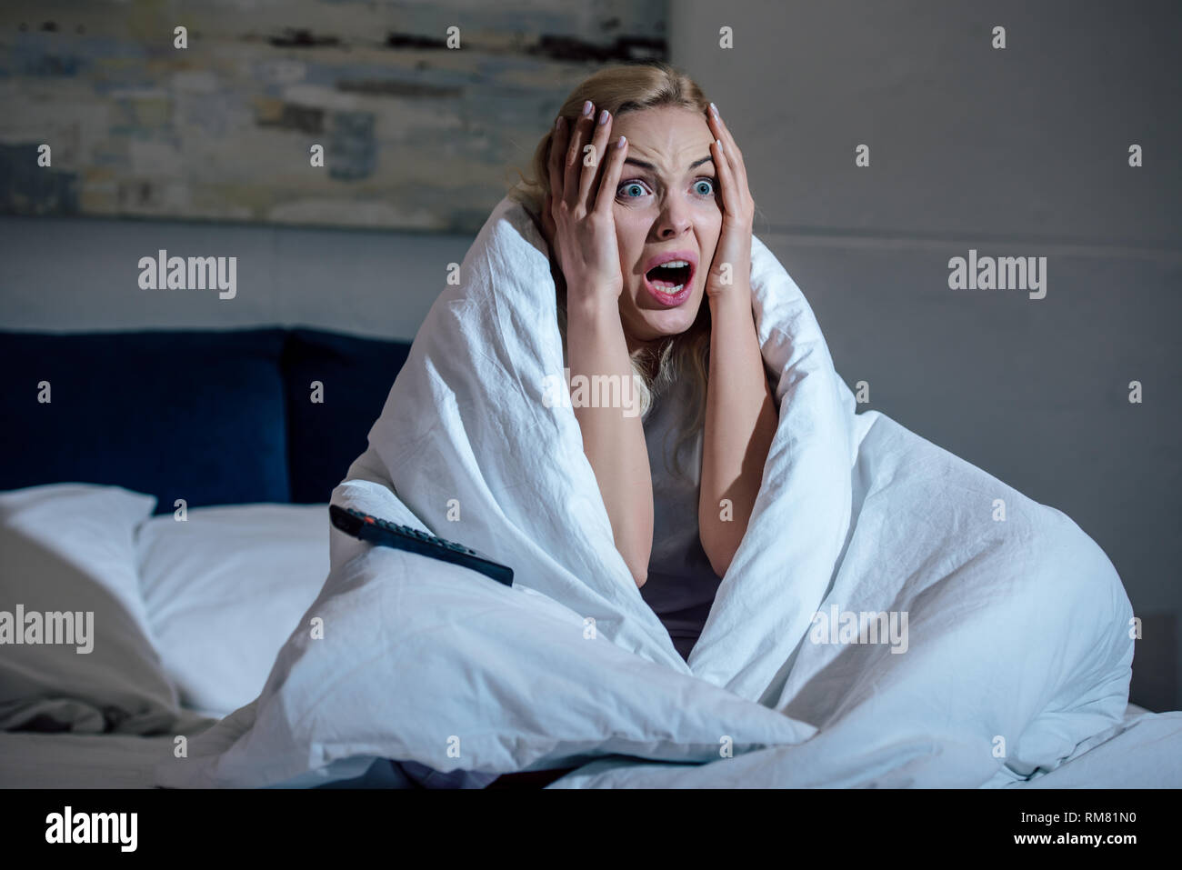 scared woman covered in blanket with hands on head screaming while ...