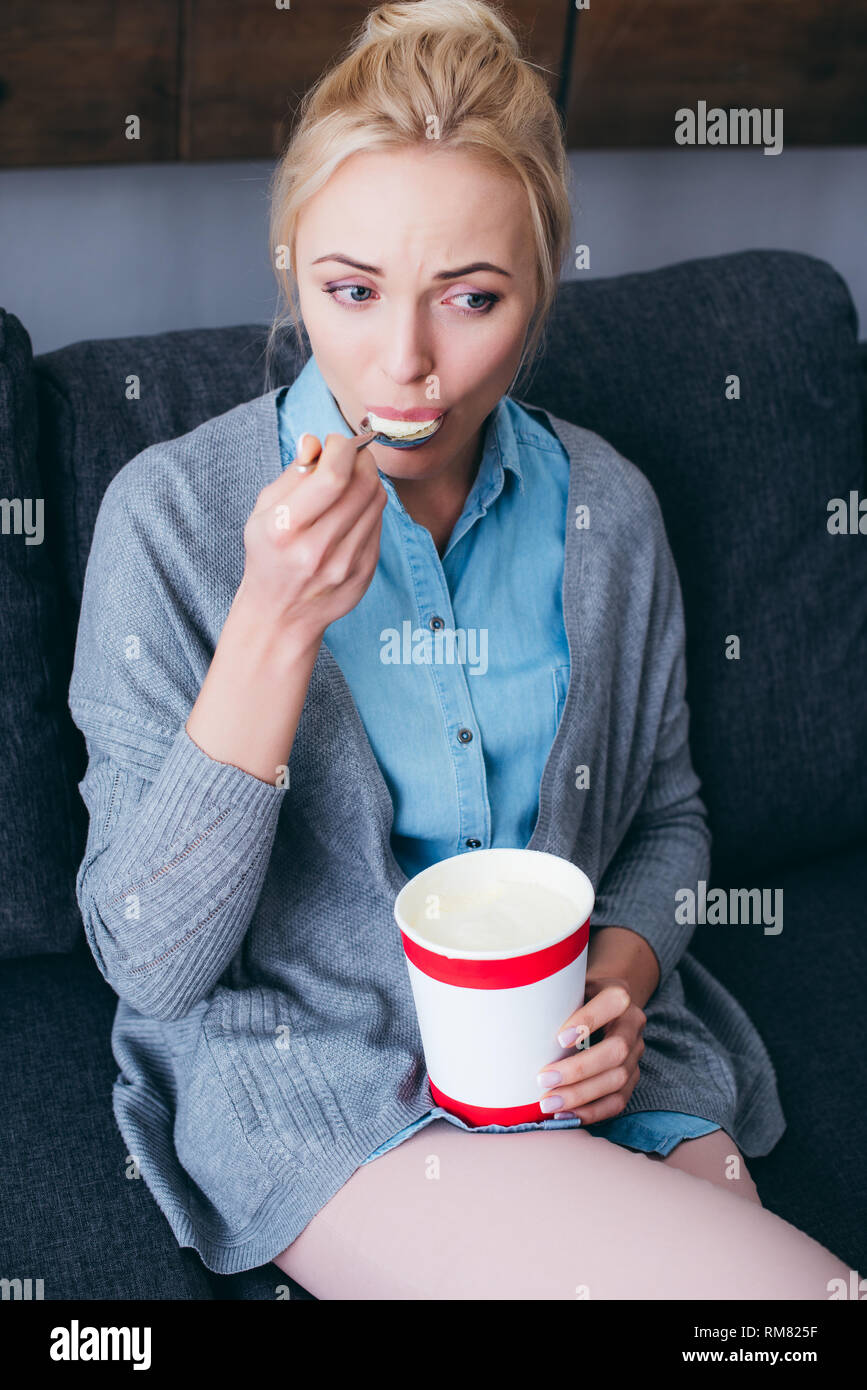 sad woman eating ice cream while siitng on couch at home alone Stock