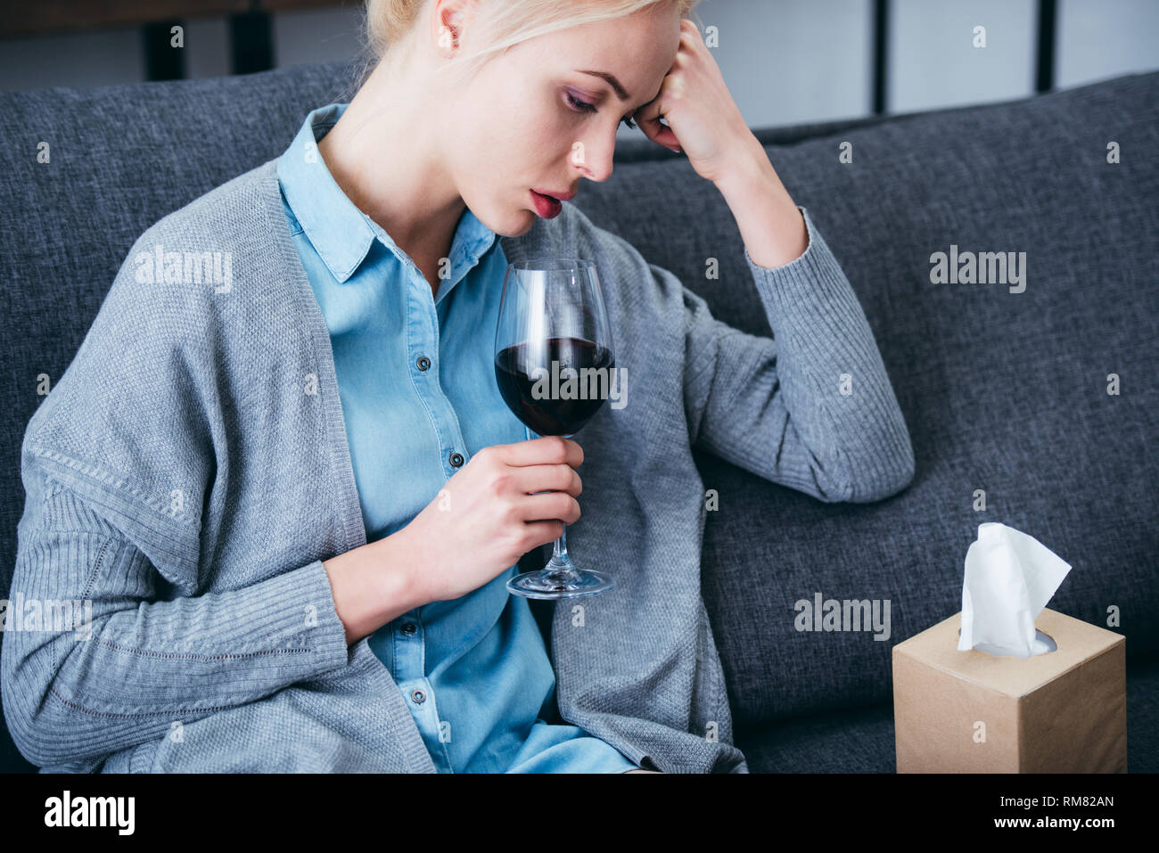 upset woman sitting with glass of red wine and tissue box at home Stock