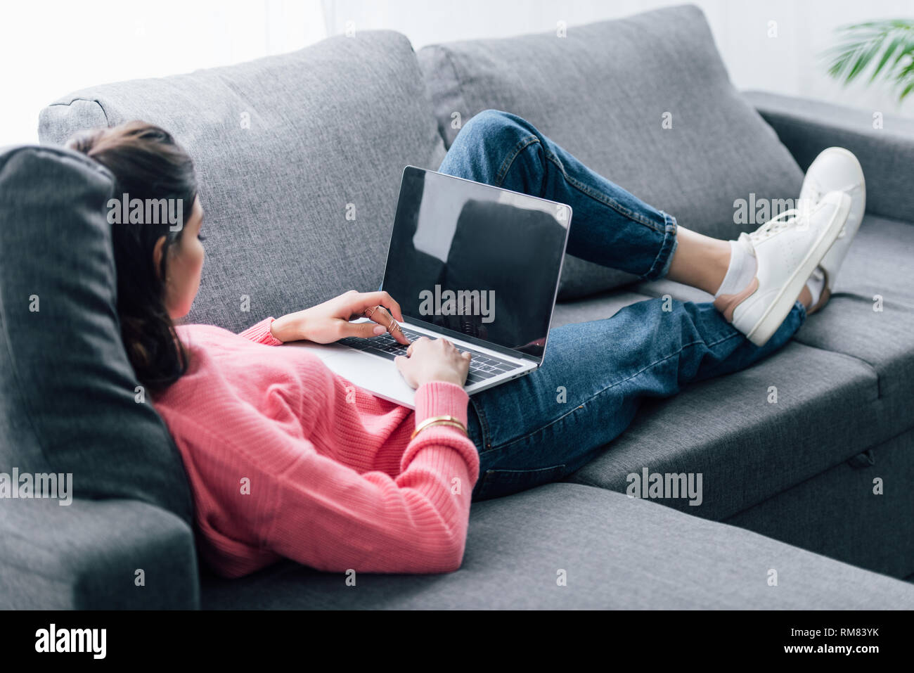 indian woman using laptop with blank screen while lying on sofa Stock Photo