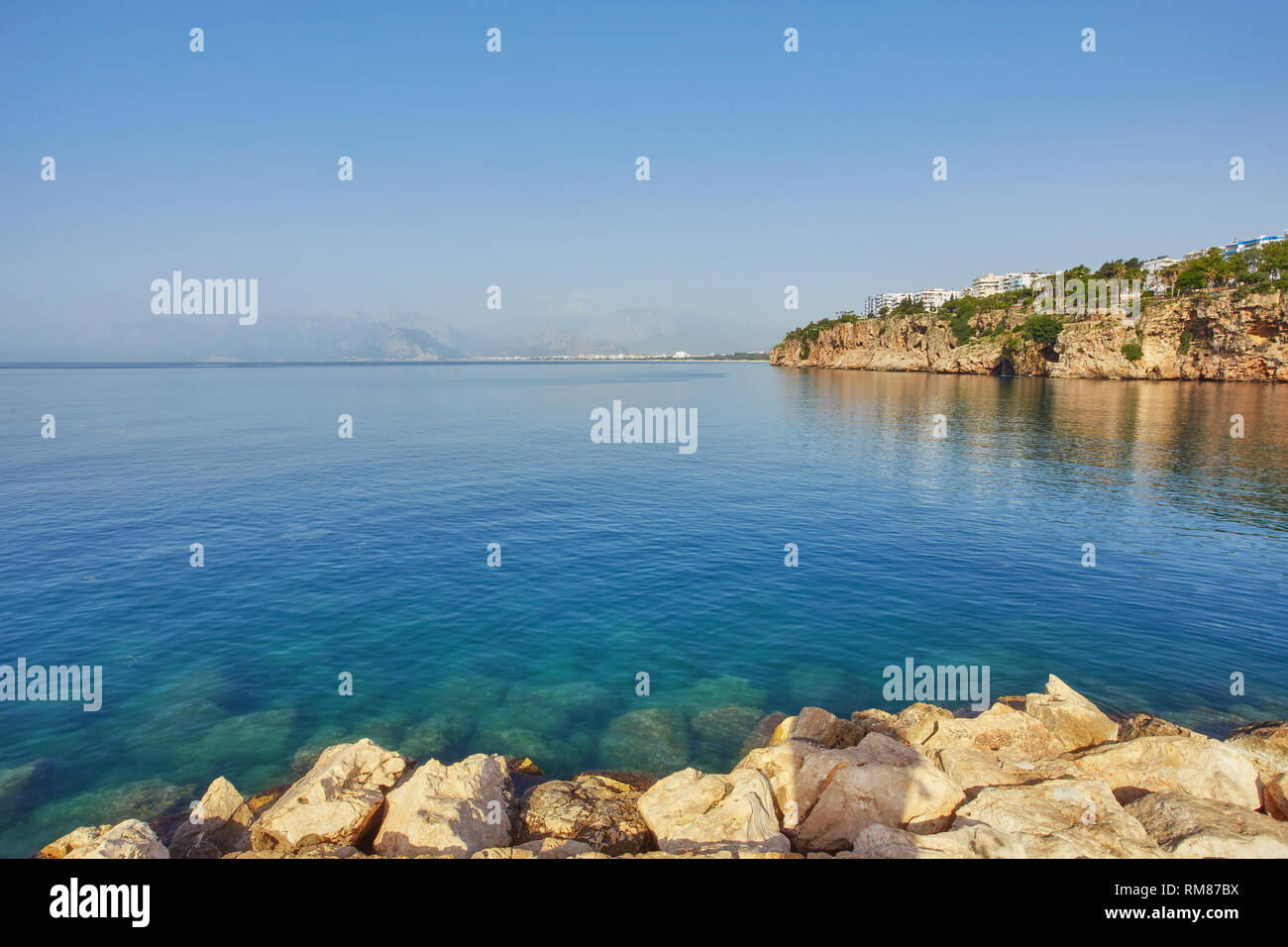 Panorama of Antalya coast from the tall cliff with Mermerli beach, Pier of old port, modern hotels and Taurus mountains on background, Turkey. Stock Photo