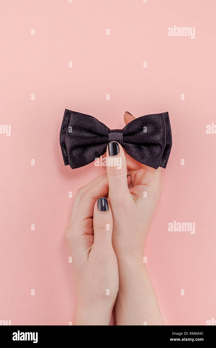 Creative flatlay top view retro black bow tie woman hands black manicure pink paper background copy space. Men health awareness month fathers day masc Stock Photo