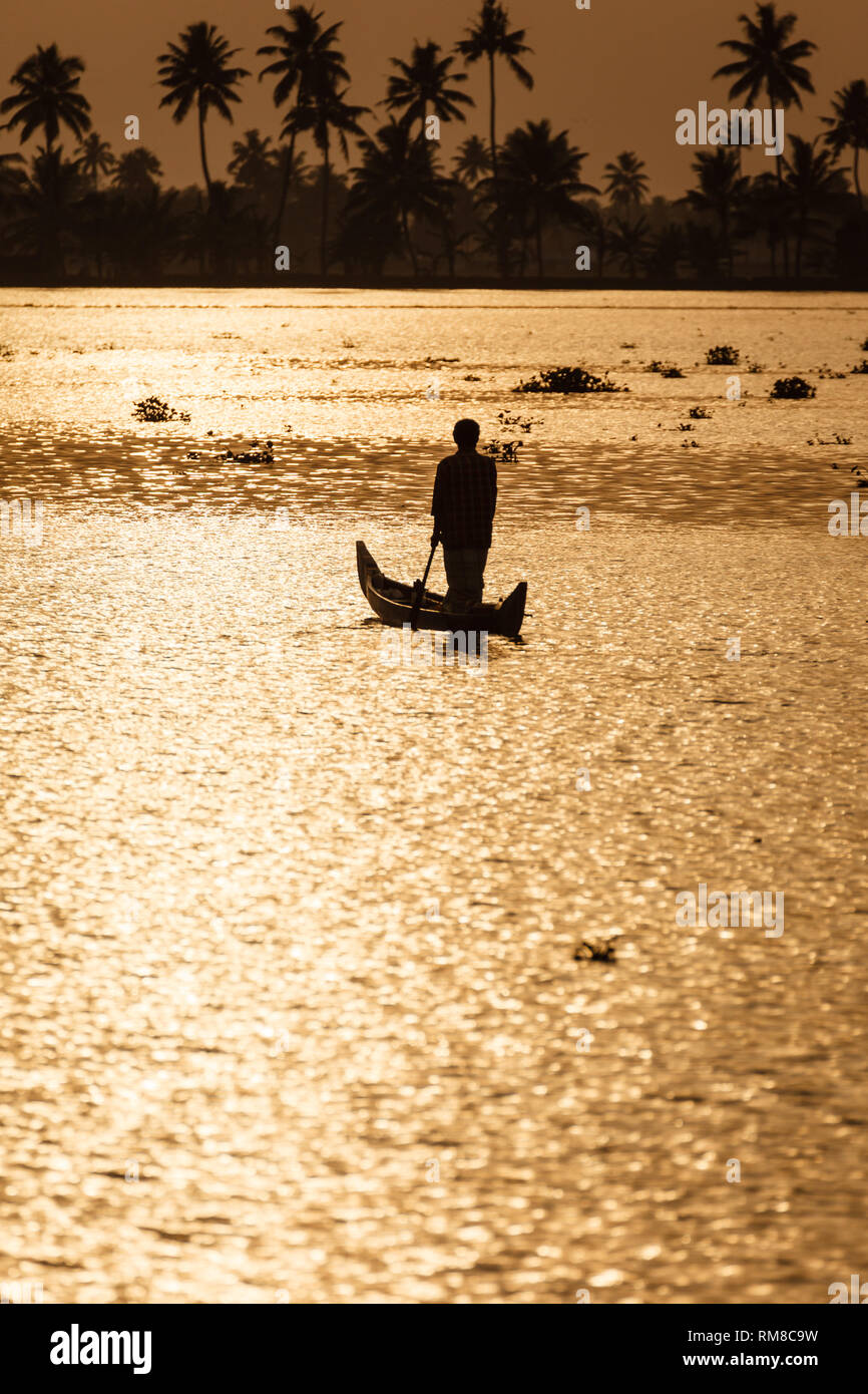 man paddling standing up in dugout canoe in sunrise lit water travels