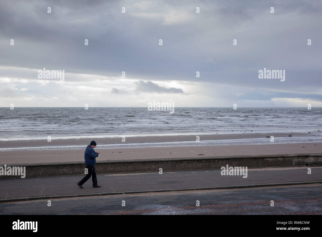 Unknown man walking The Lang Scots Mile, Ayr Promenade, ignoring the scene, looking at is mobile phone. Scotland, October 2018 Stock Photo