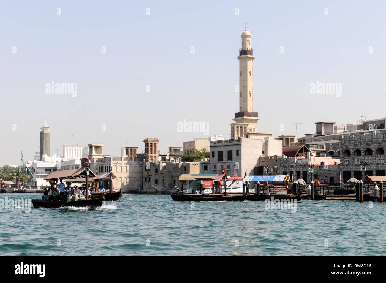 A water taxi passes near the towering minaret of the Grand Bur Dubai Masjid overlooking the Creek in the Al Souq Al Kabeer district of Dubai in the Un Stock Photo