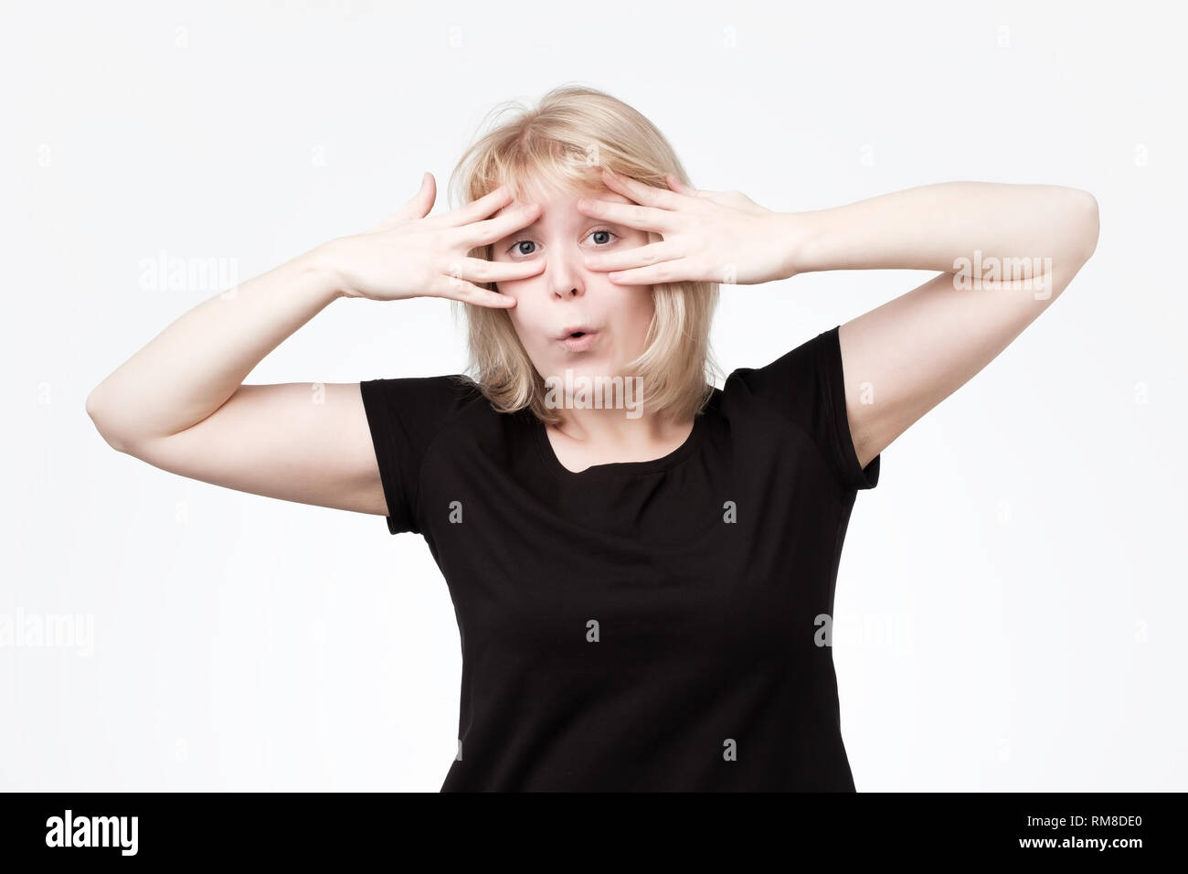 Shy timid teenage girl covering face with hands and peeping through her fingers at camera. Stock Photo