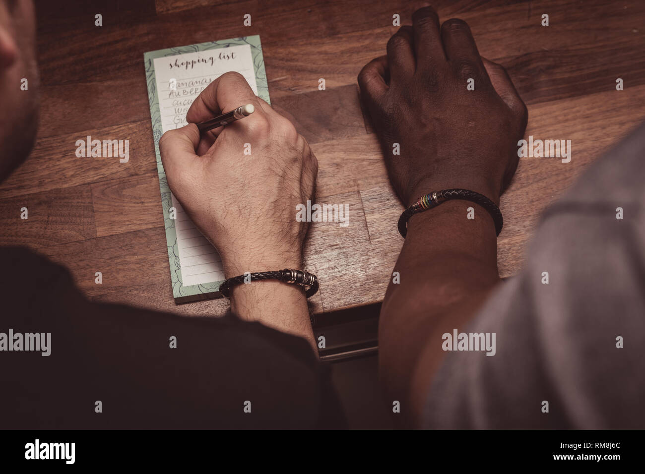 An interracial gay couple making a shopping list for groceries on a wooden kitchen top at home. Stock Photo