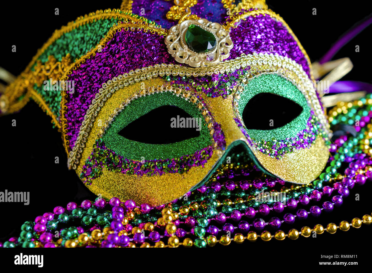 Jester carnival mask with beads in foreground on a black background. Stock Photo