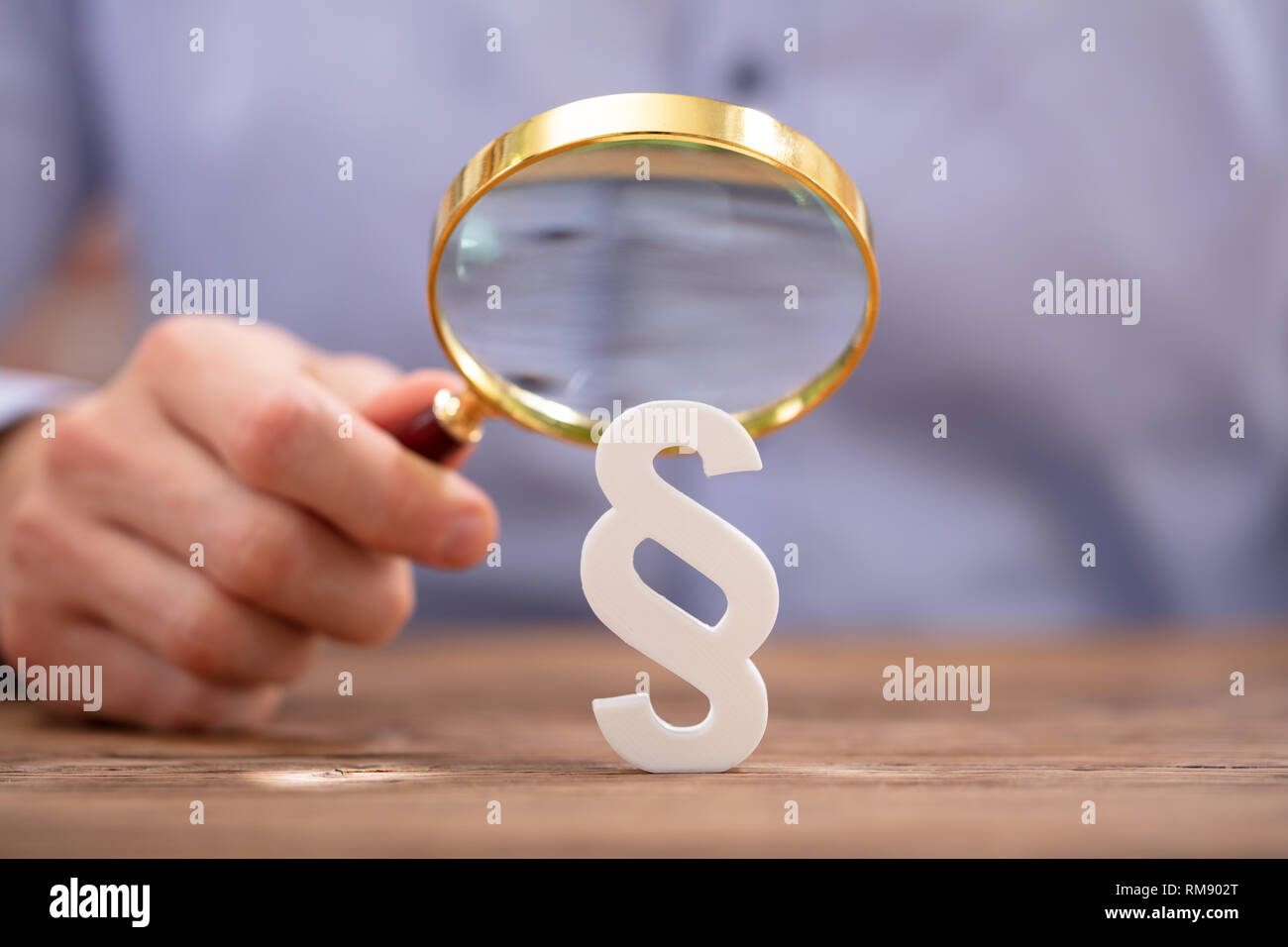 Close-up Of Businessman's Hand Looking White Paragraph Sign With Magnifying Glass On Wooden Desk Stock Photo