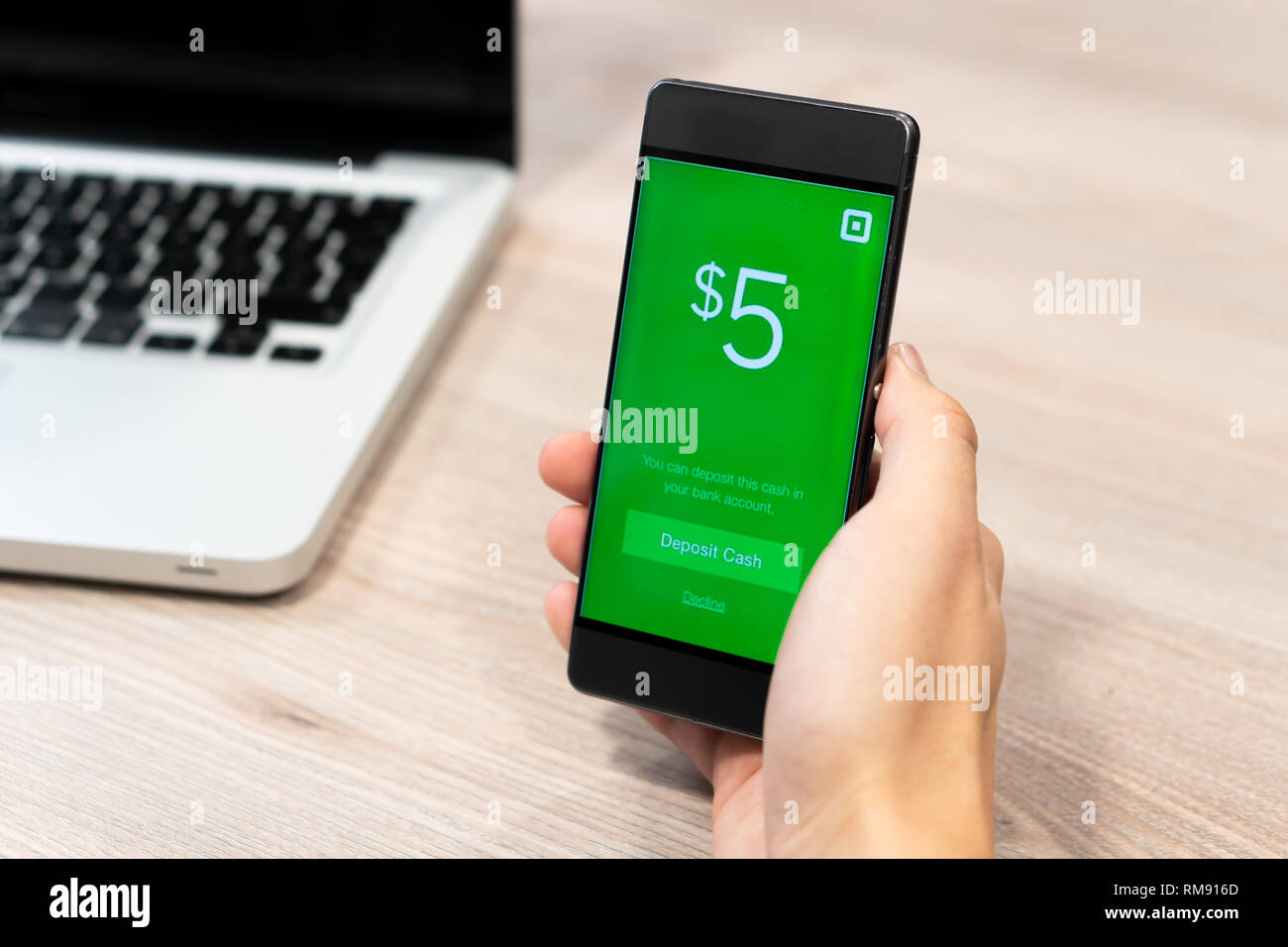 Cash App by Square inc displayed on smartphone held by human hand next to computer laptop - Slovenia 13.02.2019 Stock Photo