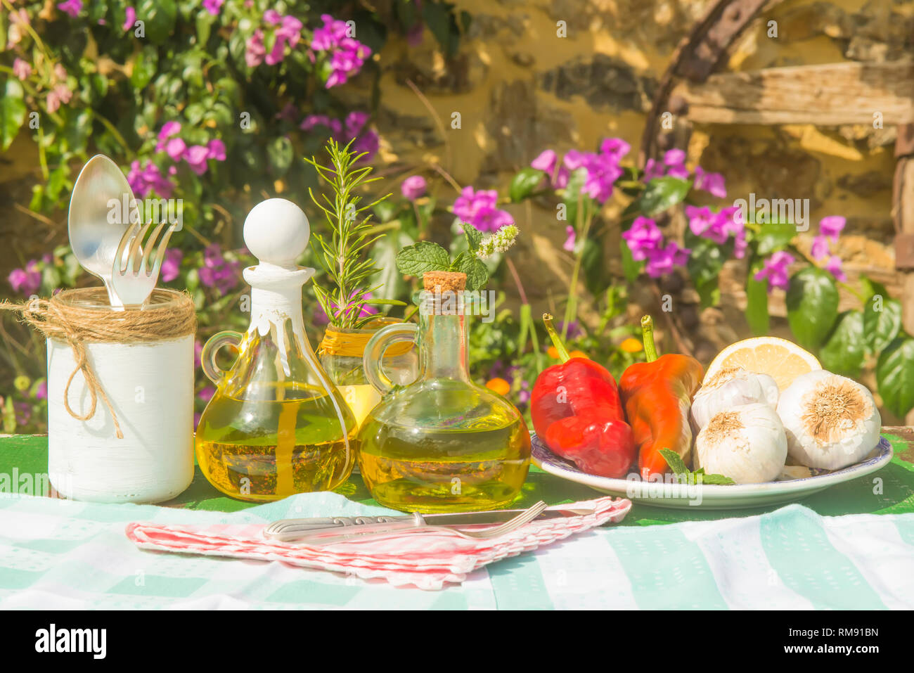 Extra virgin olive oil in vintage two glass bottles, garlic, peppers, rosemary and mint on old table in summer garden Stock Photo