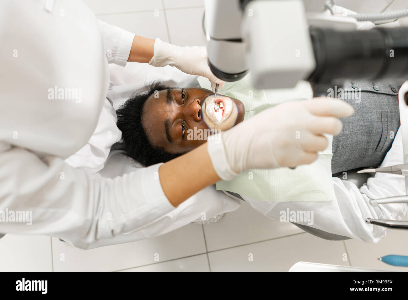 Young woman dentist treating root canals using microscope in the dental clinic. Man patient