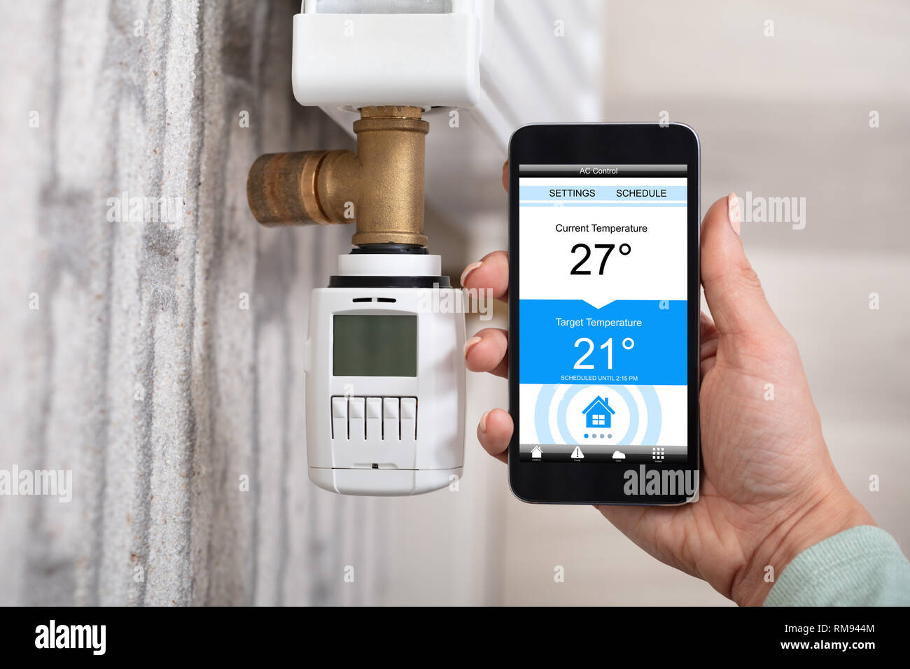 Top View Of Person's Hand Using Cellphone To Adjust Temperature Of Thermostat Stock Photo