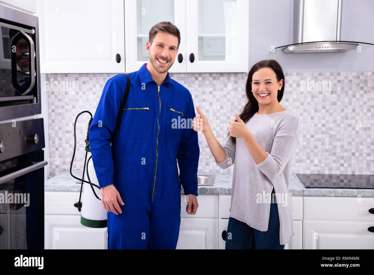 Woman Showing Thumbs Up With Pest Control Worker Standing In Kitchen Stock Photo