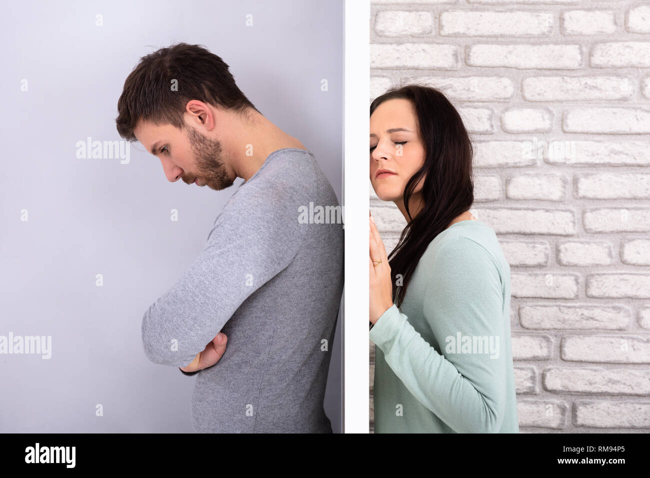 Side View Of Young Unhappy Couple Standing Back To Back At Home Stock Photo