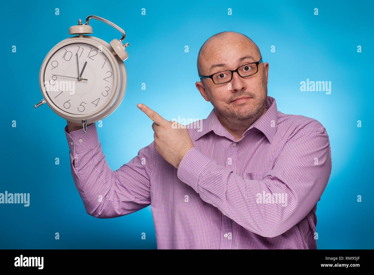 A businessman in a piked shirt pointing with the index finger on a huge alarm clock,  on the blue background. Stock Photo