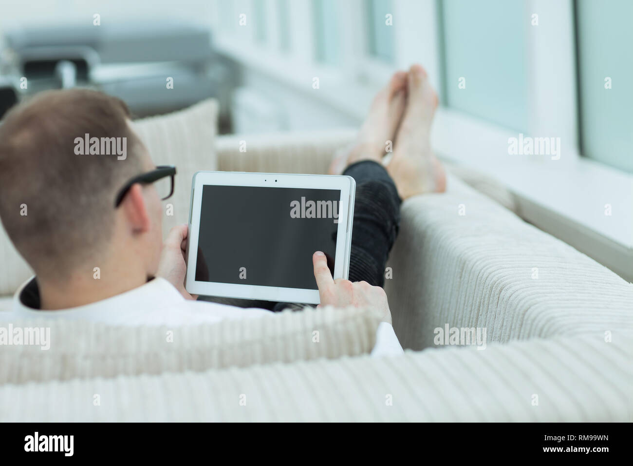 rear view.a young man with a digital tablet sitting on a couch in his living room Stock Photo