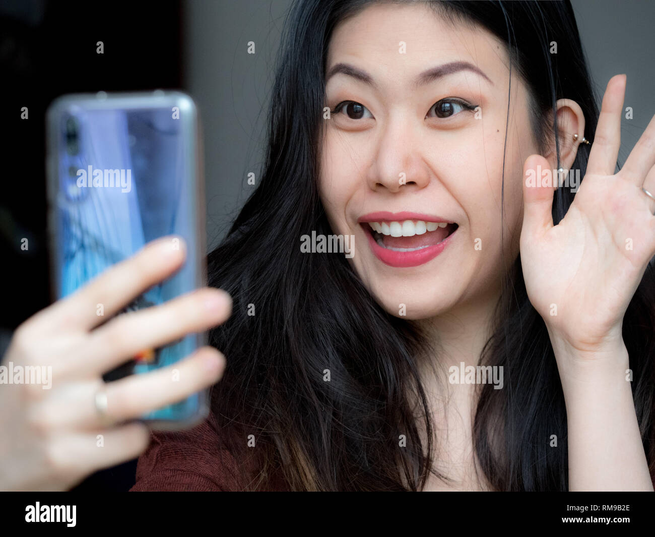 Asian young beautiful cheerful woman smiling, waving and saying hi to