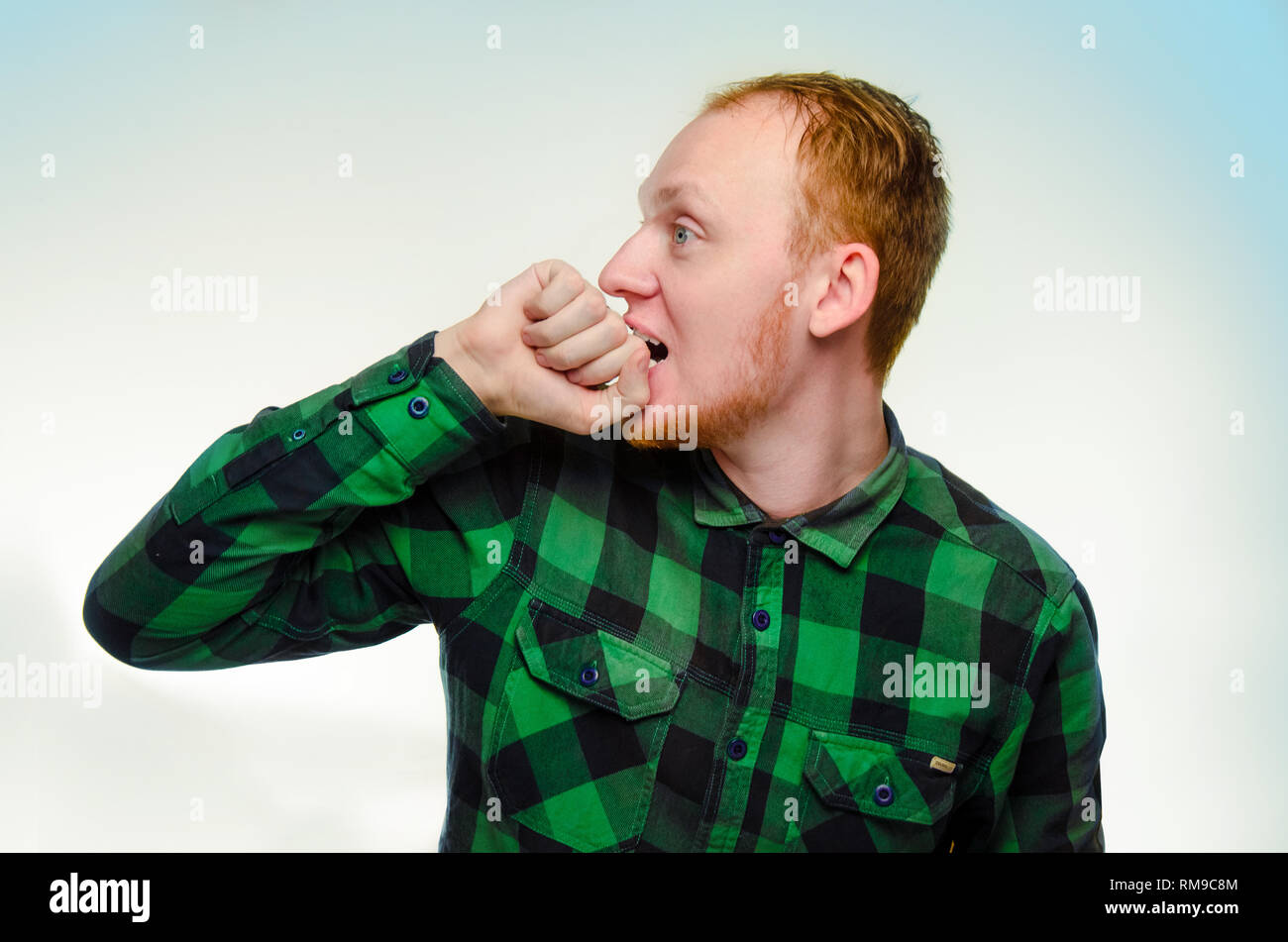 red haired man bite his fist, hand. shocked, caucasian male teenager. surprised redhead guy scream. reaction to surprise is overjoyed shock. emotion is serious, fear, stress. Stock Photo