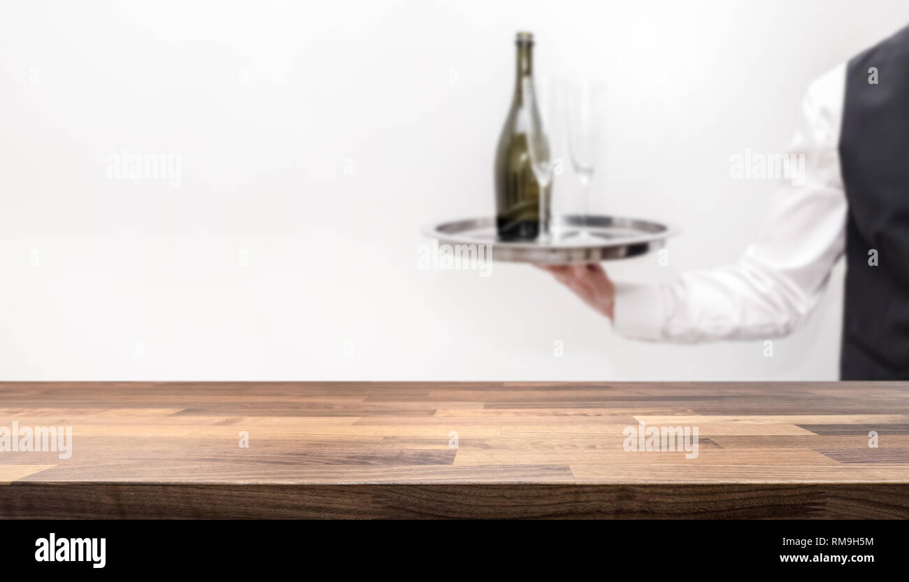 Empty table top for product display montage. Waiter / butler in white shirt and black suit vest carrying an silver tray with a bottle of champagne and Stock Photo