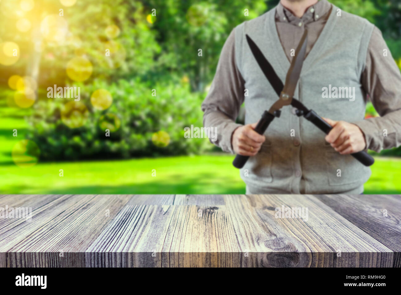 Empty table top for product display montage. Gardener holding a hedgecutter blurred in the background. Gardening concept. Stock Photo