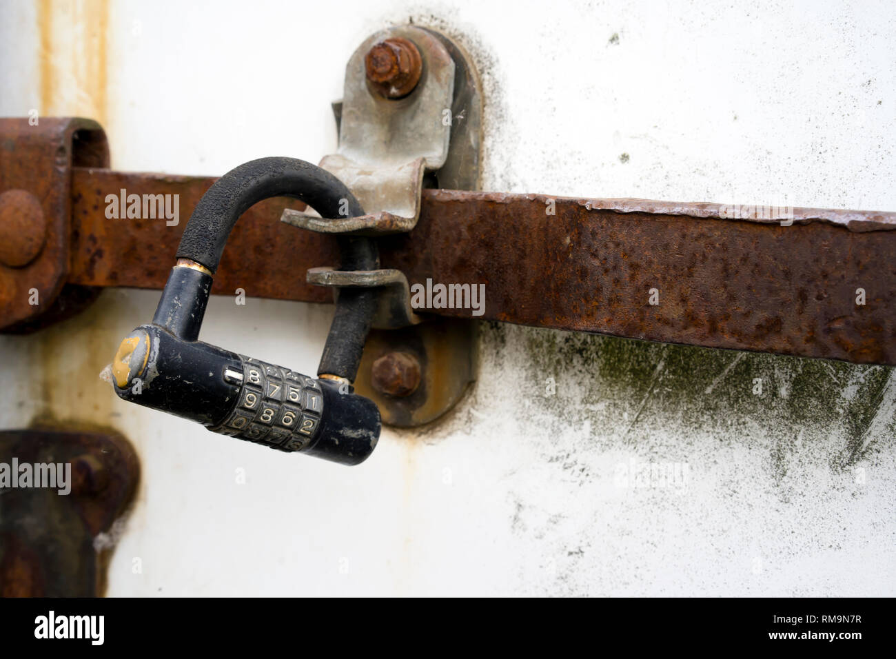 An old digital dial-padded combination padlock keeps the deadbolt on the doors of an old rusted semi trailer from unauthorized access to the goods sto Stock Photo